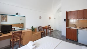 Habitación de hotel con cama, escritorio, silla, mesita pequeña y una kitchenette.