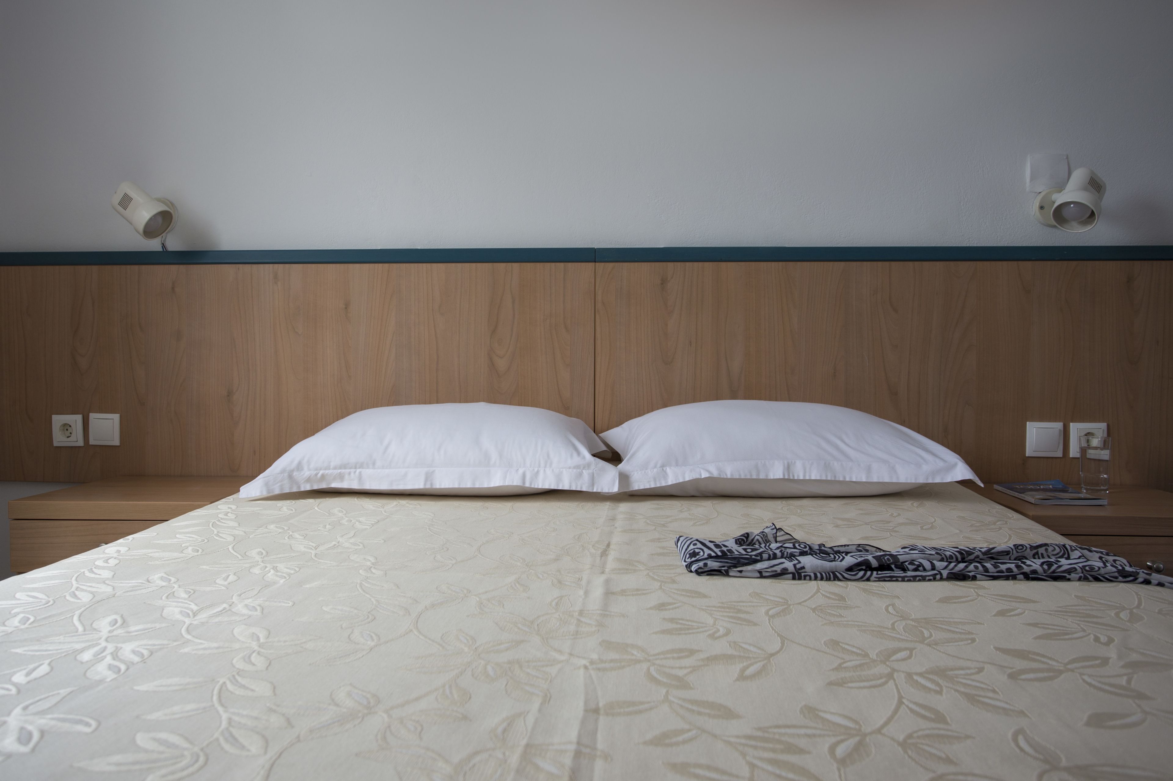 Un lit bien fait, recouvert d’une couvre-lit à motifs floraux, avec deux oreillers blancs et un plaid à motifs.