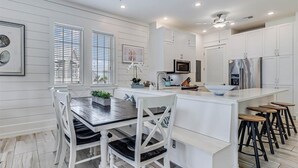 A modern kitchen with white cabinetry, a central island with stools, and a dining table with chairs. - Stylish, Beachy Condo near Many Resort-Like Amenities@Cinnamon Shore (Port Aransas)