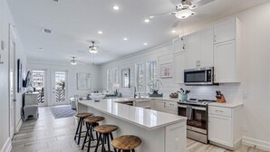 A modern kitchen with white cabinetry, a central island with stools, a microwave, and an oven. - Stylish, Beachy Condo near Many Resort-Like Amenities@Cinnamon Shore (Port Aransas)