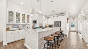A spacious kitchen with white cabinetry, a large island with stools, and a view to the outside. - Gracious Home w/ Lake Views, Fire Pit, and More Amenities in Cinnamon Shore (Port Aransas)