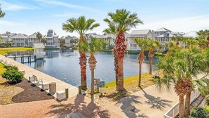 A waterfront property with a dock, palm trees, and a row of houses. - Gracious Home w/ Lake Views, Fire Pit, and More Amenities in Cinnamon Shore (Port Aransas)