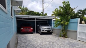 A garage with two cars parked inside, a paved driveway, and a white picket fence. - 2 minute Walk to Beach, Newly Renovated, 2 Bed 2 Bath Apartment #1
Shenstone (Rockley)