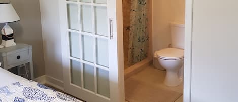 A bedroom with a bed, a nightstand, a bathroom with a toilet, and a shower.