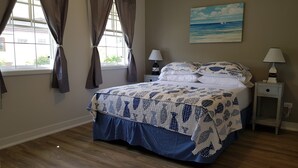 A bedroom with a bed, two bedside lamps, a painting on the wall, and a window with curtains. - 2 minute Walk to Beach, Newly Renovated, 2 Bed 2 Bath Apartment #1
Shenstone (Rockley)