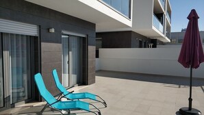 A modern building with a balcony, two blue lounge chairs, and a purple umbrella.