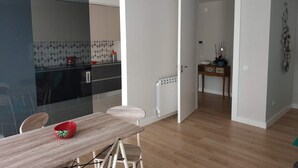 A modern kitchen with a glass partition, a dining area with a wooden table and chairs, and a small side table with decorative items.