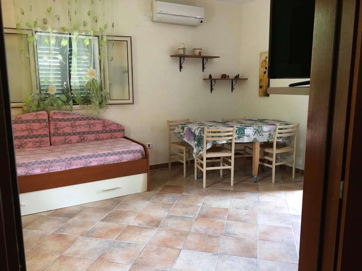 Una habitación con cama, una mesa de comedor con sillas, un televisor y una ventana con persianas.