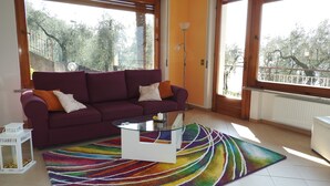 A living room with a purple sofa, a glass coffee table, and a colorful rug. - Apartment in Malcesine on Lake Garda. New, with panoramic Parking. (Malcesine)