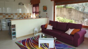 A modern kitchen with white cabinets, a gas stove, and a dining area with a purple sofa and a glass coffee table. - Apartment in Malcesine on Lake Garda. New, with panoramic Parking. (Malcesine)
