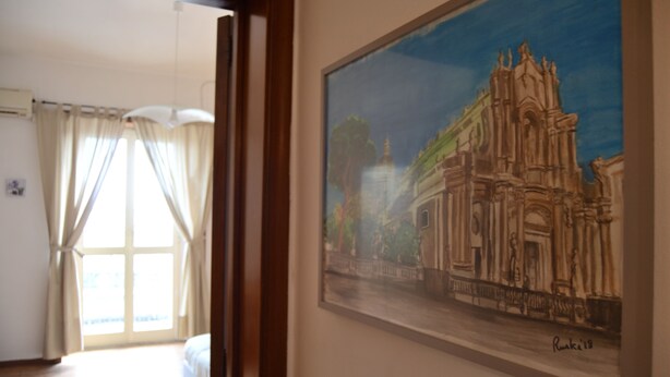 A room with a large window, a bed, and a framed painting of a building. - Street Art House (Catania)
