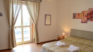 A hotel room with a bed, curtains, a nightstand, a lamp, and a window with a view. - Street Art House (Catania)