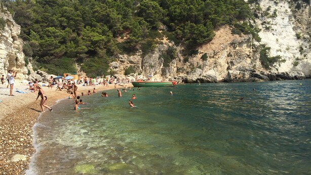 Una playa con agua cristalina, acantilados rocosos y un barco llamado "Bacardi".