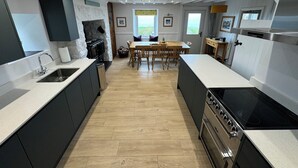 A modern kitchen with a central island, built-in oven, and a dining area with a wooden table and chairs. - Amazing sea views Set in 7 acres of fields Dog friendly On the welsh coast path. (Nefyn)