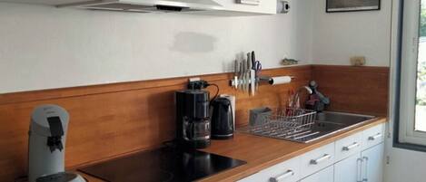 A modern kitchen with white cabinets, a wooden countertop, a built-in dishwasher, and a coffee maker.