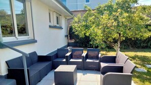 An outdoor seating area with wicker furniture, a tree, and a house in the background. - House / Villa - Agon Coutainville (Agon-Coutainville)