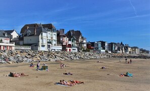 A beach with people sunbathing and swimming, and colorful houses in the background.