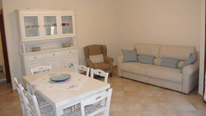 A living room with a beige sofa, a dining table with chairs, and a white cabinet with glass doors.