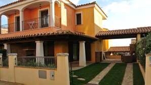 A two-story house with a balcony, a patio with outdoor furniture, and a well-maintained lawn.