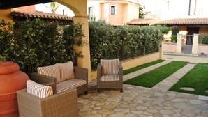 An outdoor patio with wicker furniture, stone flooring, and a well-maintained hedge.