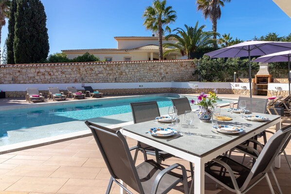 A poolside dining area with a stone wall, lounge chairs, and a table set for two.