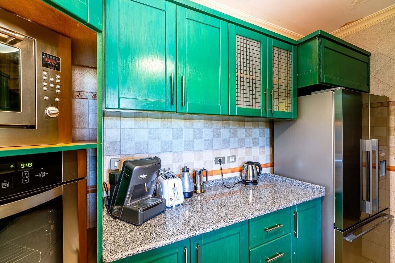 A kitchen with green cabinets, a stainless steel microwave, a coffee maker, and a refrigerator.