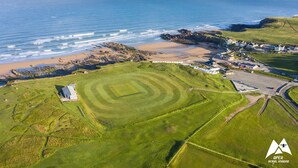 An aerial view of a coastal area with a golf course, beach, and residential buildings. - Stunning luxury cliff top retreat - direct access to the South West Coast Path. (Bude)