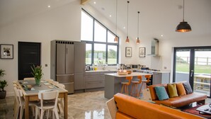 A modern kitchen with a dining area, a large window, and a seating area with a sofa. - Stunning luxury cliff top retreat - direct access to the South West Coast Path. (Bude)
