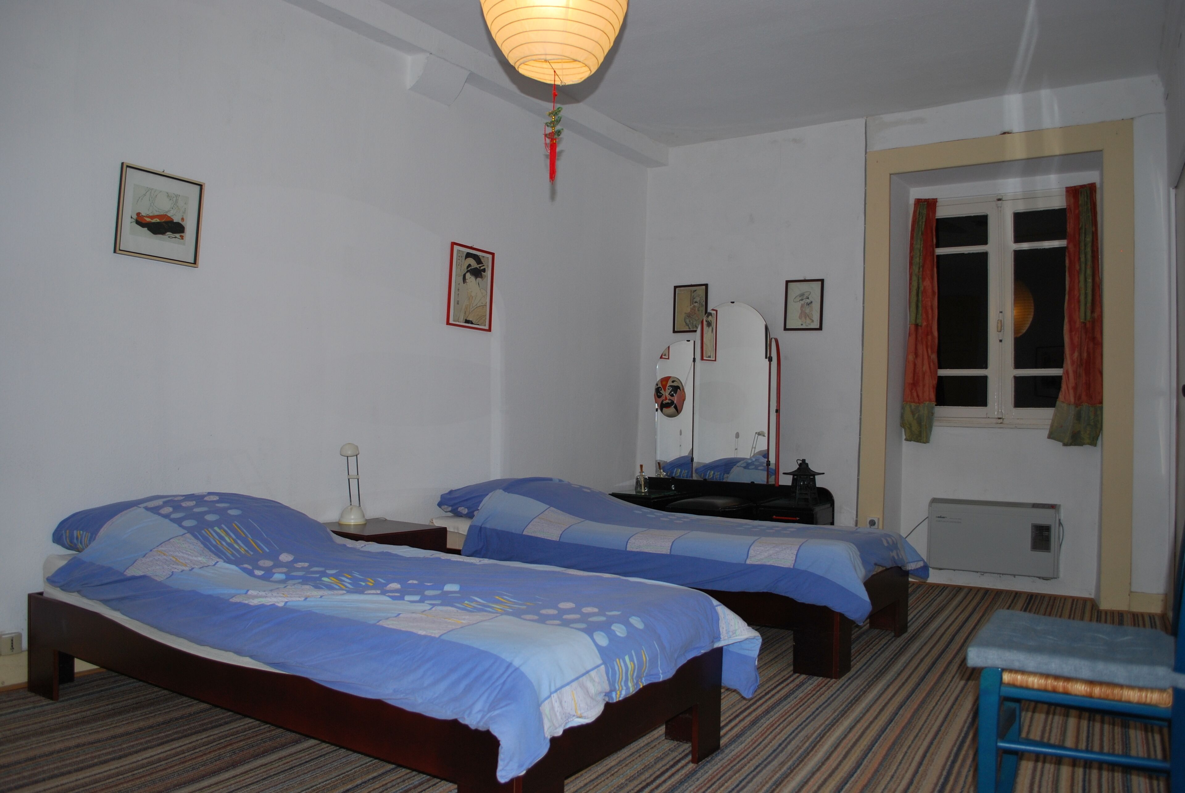 Habitación de hotel con dos camas, una mesita de noche, una silla y una ventana con cortinas.