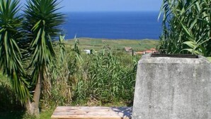 A stone barbecue grill with a wooden picnic table in a grassy area with a view of the ocean. - Country Cottage - Cedros, typical Azorien Big House with garden and seaview (Cedros)