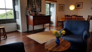A living room with a blue armchair, wooden coffee table, and a desk with books. There is a dining table with chairs in the background. - Country Cottage - Cedros, typical Azorien Big House with garden and seaview (Cedros)