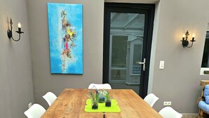 A conference room with a large wooden table, white chairs, a painting on the wall, and a door leading outside.