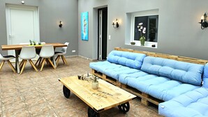 A room with a wooden table, white chairs, a blue sofa, and a glass ceiling.