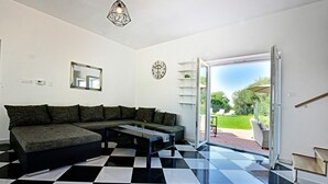 A modern living room with a black and white checkered floor, a sectional sofa, a coffee table, a pendant light, a wall clock, and a sliding glass door leading to an outdoor area with a garden view. - Stylish Casa Lavanda with private pool and garden in Vrsar (Vrsar)