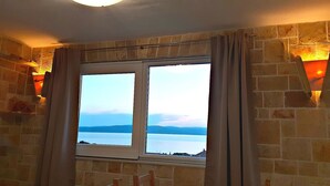 A room with a large window overlooking a body of water and distant hills.