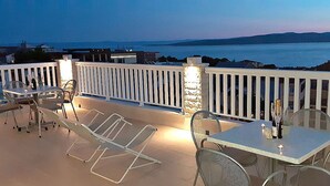 A terrace with outdoor seating, a stone pillar, and a view of the sea.