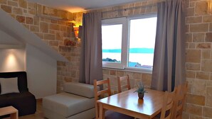 A cozy room with a stone wall, a wooden table with chairs, a sofa, and a window with curtains.