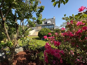 A house with a modern design, a well-maintained garden with pink flowers, and a clear sky.
