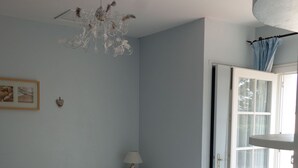 Une chambre à coucher comprenant un lit, une table de chevet, une lampe, un lustre et une porte donnant sur un balcon.