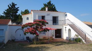 Un bâtiment blanc à deux étages, doté d’un balcon, d’un escalier et d’une table de pique-nique dans le jardin avant.
