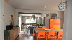A modern kitchen with a dining area, featuring a large island, orange chairs, and a clock on the wall. -  Villa for 8 persons with a brand new pool, large garden area, close to the Isle (L'isle-Sur-La-Sorgue)