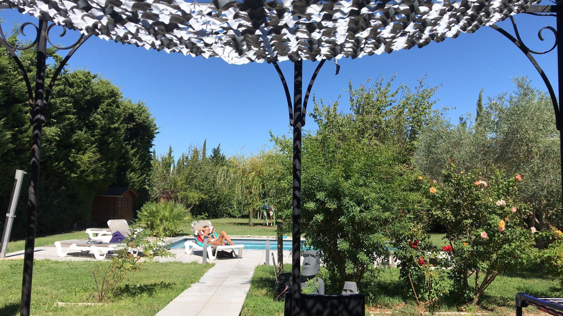 A poolside area with lounge chairs, a pool, and a pergola with white foliage.