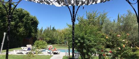 A poolside area with lounge chairs, a pool, and a pergola with white foliage.