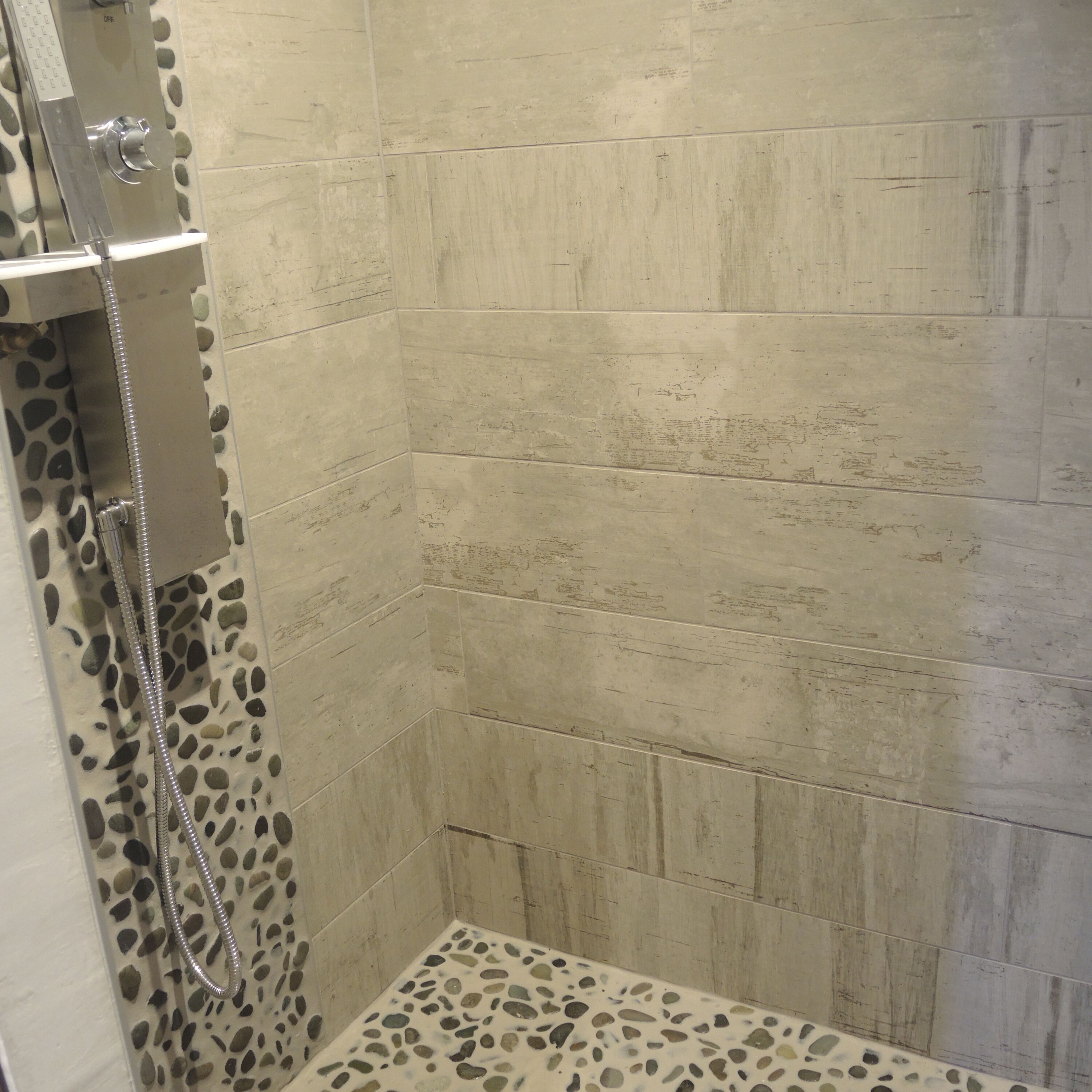 Une douche avec un sol décoré de motifs de galets et une pomme de douche en métal.