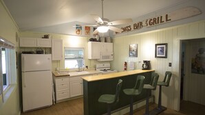 Eine Küche mit Barbereich und Grill, weißen Schränken, einem Kühlschrank, einer Spüle, einem Herd und grünen Barhocker.