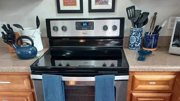 A kitchen with a stainless steel stove, wooden cabinets, and a blue kettle.
