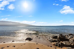 Una playa con cielos despejados, agua tranquila y costa rocosa.