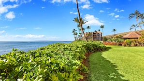 A beachfront hotel with a well-maintained lawn, palm trees, and a view of the ocean. - Wake, Sip and Savor the Views in Your 2BR Escape (Wailuku)