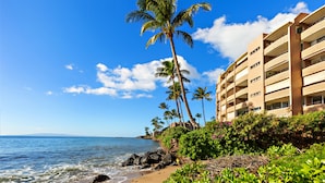 A beachfront hotel with multiple balconies, a palm tree, and a clear blue sky. - Wake, Sip and Savor the Views in Your 2BR Escape (Wailuku)