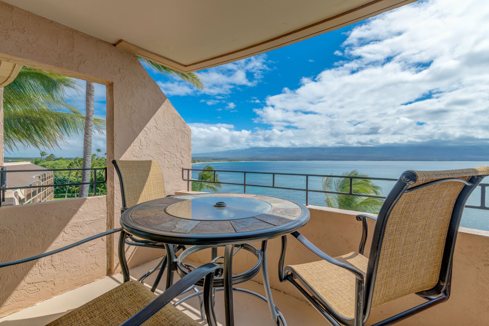 Un balcon avec une table ronde et des chaises, offrant une vue panoramique sur l’océan.